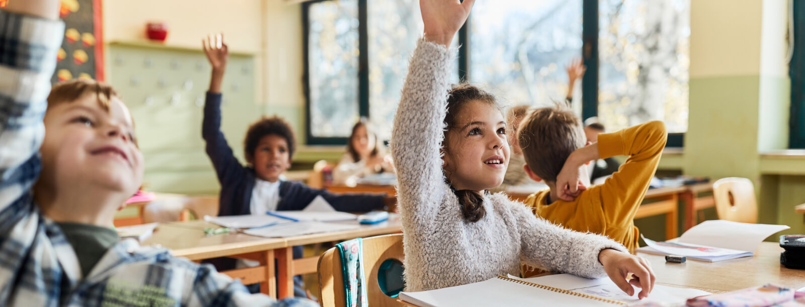 Young kids raising their hands in a classroom